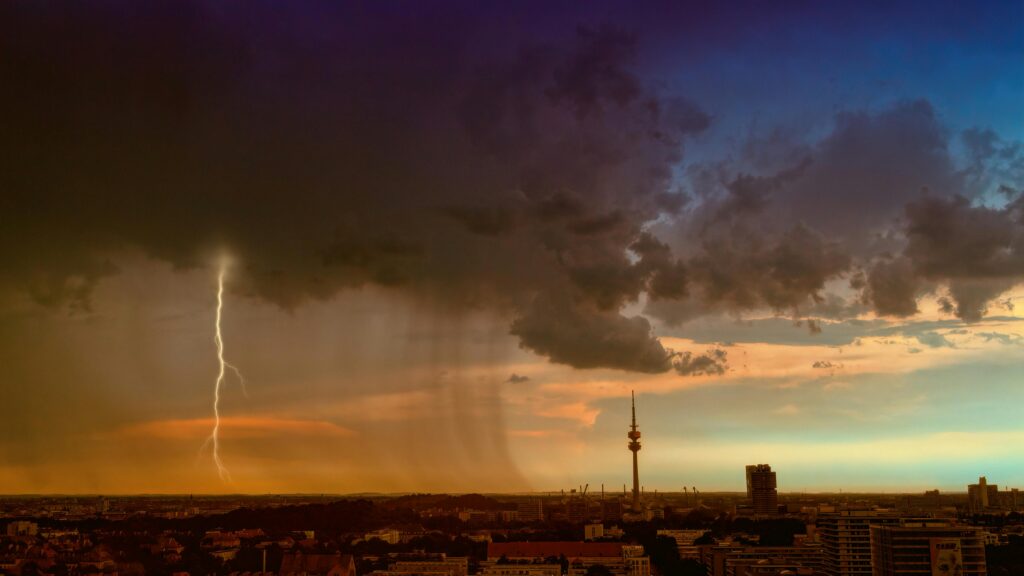 Visão panorâmica de nuvem com raio e chuva caindo com fundo do céu em pôr-do-sol e metrópole com prédios